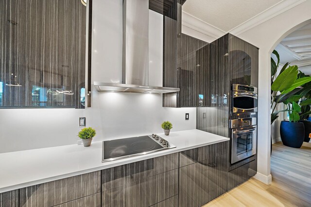 kitchen featuring wall chimney exhaust hood, electric cooktop, modern cabinets, light wood-style flooring, and ornamental molding