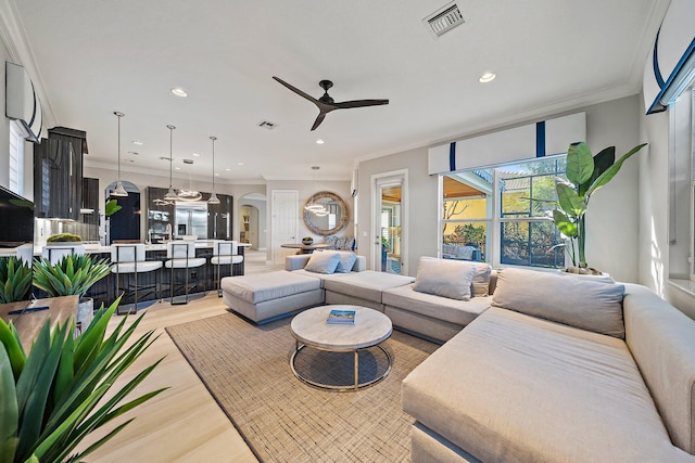 living room featuring ceiling fan, arched walkways, crown molding, light wood-style floors, and recessed lighting