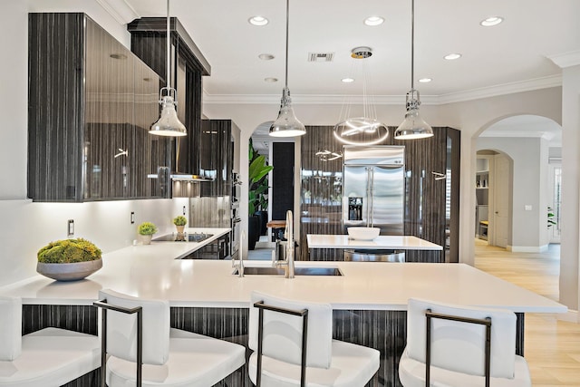 kitchen featuring stainless steel built in fridge, a sink, arched walkways, light countertops, and pendant lighting