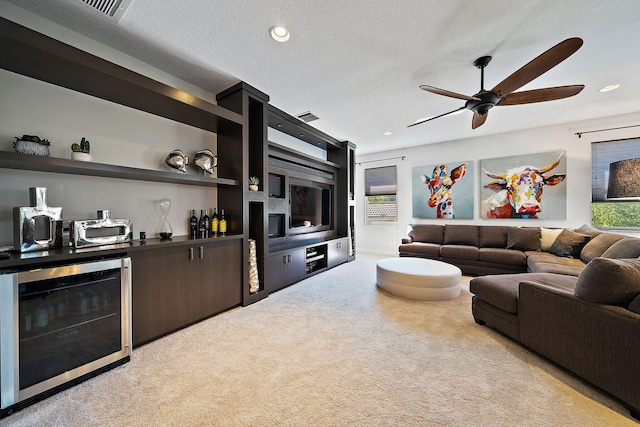 living room with beverage cooler, a bar, light colored carpet, a ceiling fan, and a textured ceiling