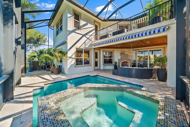 back of house featuring a balcony, a patio area, stucco siding, a pool with connected hot tub, and an outdoor living space with a fireplace