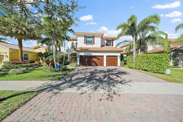 mediterranean / spanish home with decorative driveway, an attached garage, a tiled roof, and stucco siding