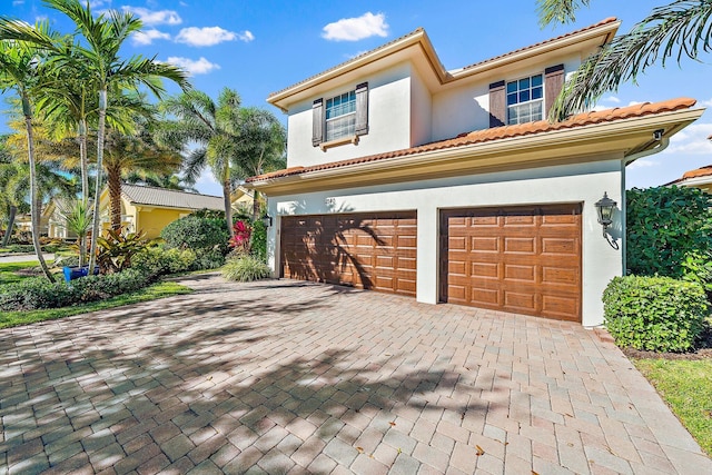 view of front facade featuring a garage, stucco siding, decorative driveway, and a tile roof