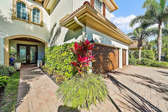 property entrance with french doors, stucco siding, a garage, and driveway