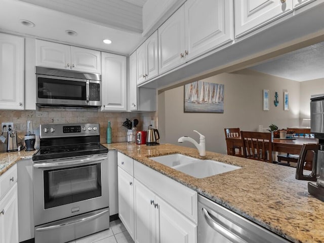 kitchen with appliances with stainless steel finishes, a sink, light stone counters, white cabinetry, and recessed lighting
