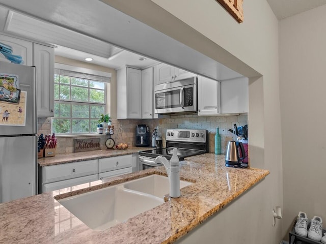 kitchen with stainless steel appliances, white cabinets, backsplash, light stone countertops, and a sink