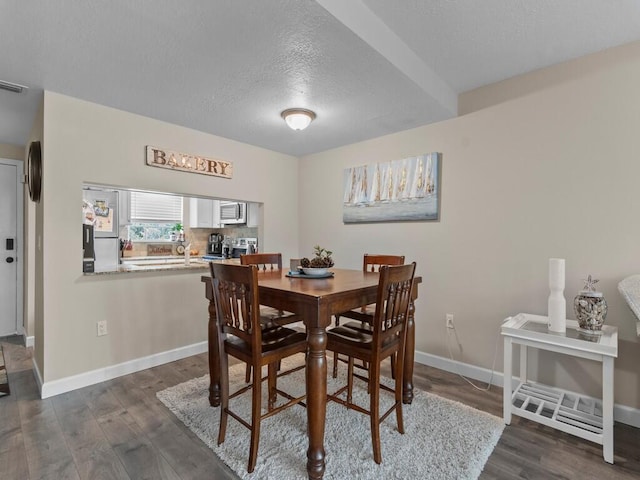 dining area with dark wood-style flooring, a textured ceiling, and baseboards