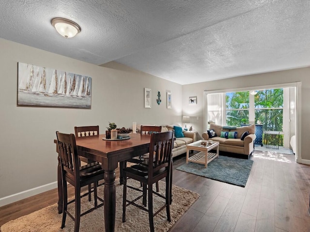 dining room featuring a textured ceiling, wood finished floors, and baseboards