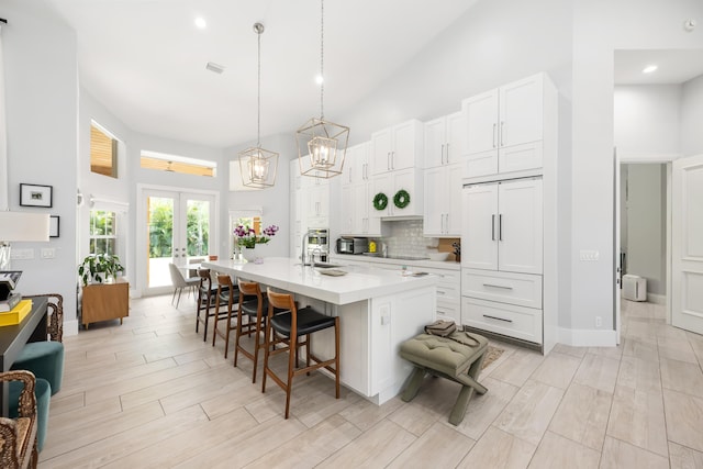 kitchen featuring high vaulted ceiling, decorative backsplash, a kitchen bar, french doors, and light countertops