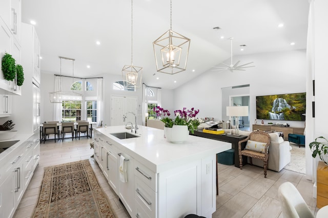 kitchen featuring a sink, light countertops, white cabinets, a kitchen island with sink, and pendant lighting
