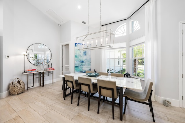 dining room featuring a high ceiling, a chandelier, baseboards, and light wood finished floors