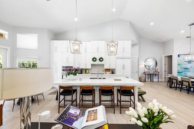 kitchen featuring high vaulted ceiling, an island with sink, light countertops, backsplash, and a sink