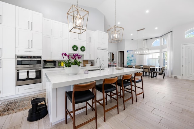 kitchen featuring high vaulted ceiling, a sink, a chandelier, stainless steel double oven, and a kitchen bar