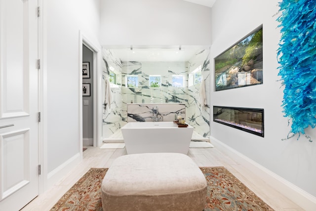 bathroom featuring a marble finish shower, a glass covered fireplace, and a soaking tub