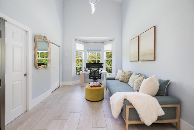 living area featuring a towering ceiling, light wood finished floors, and baseboards