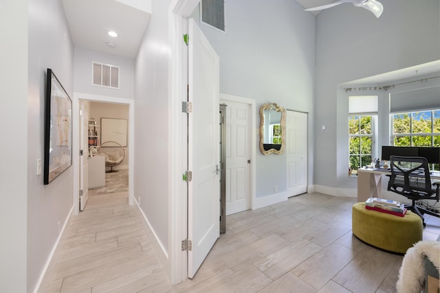 hallway featuring a towering ceiling, baseboards, a desk, and light wood-type flooring