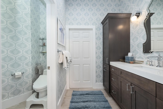 bathroom with wallpapered walls, toilet, vanity, and baseboards