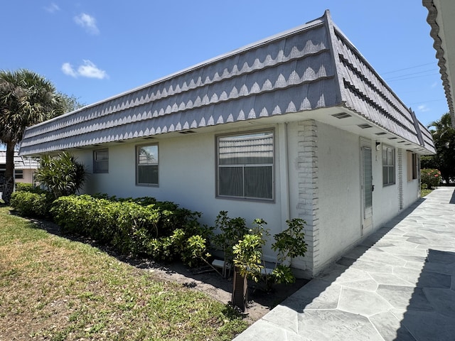 view of side of home featuring mansard roof and stucco siding