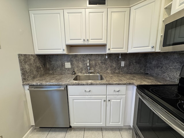 kitchen featuring appliances with stainless steel finishes, a sink, light tile patterned floors, and white cabinets
