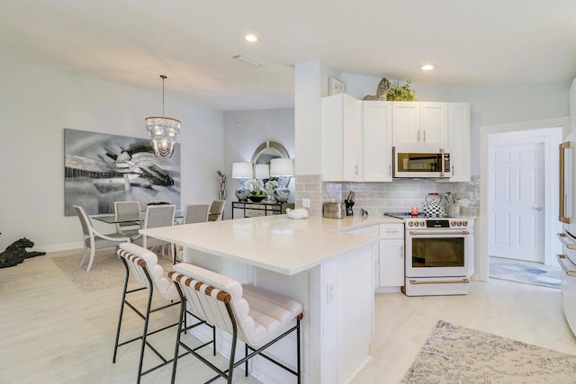 5021 Magnolia Bay Cir, Palm Beach Gardens, FL 33418 - kitchen featuring white appliances, a peninsula, a breakfast bar, light wood-style floors, and white cabinets