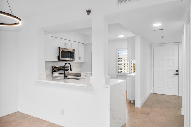 kitchen with appliances with stainless steel finishes, light countertops, white cabinetry, a peninsula, and baseboards