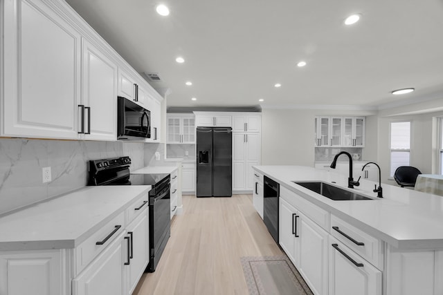 kitchen featuring black appliances, a sink, recessed lighting, decorative backsplash, and glass insert cabinets