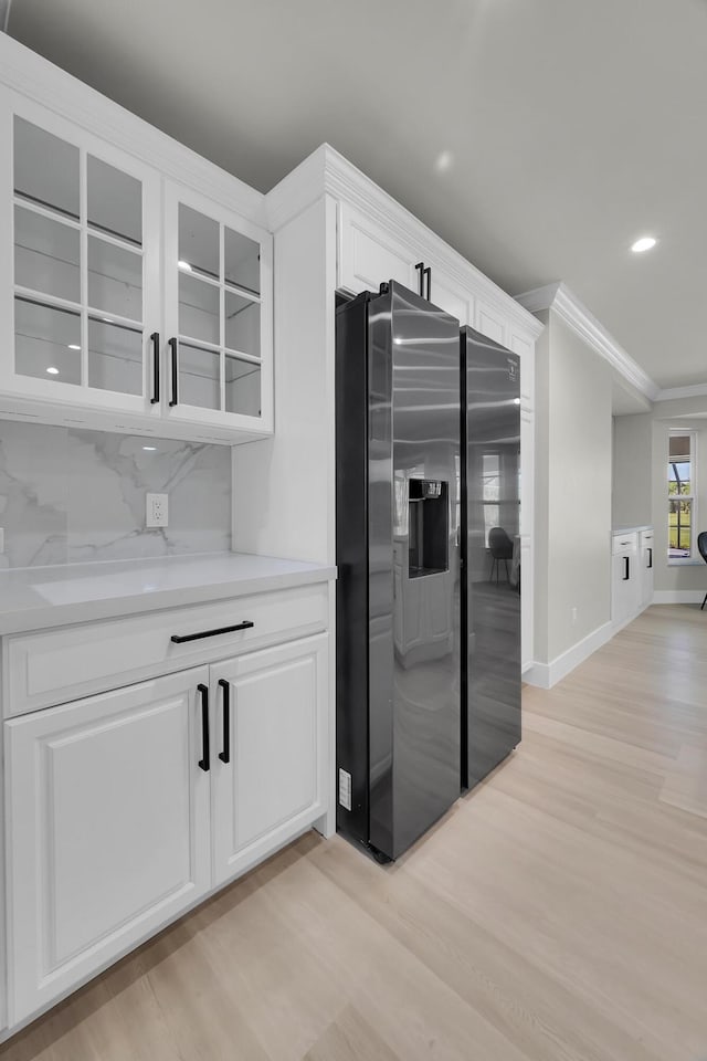 kitchen with stainless steel refrigerator with ice dispenser, light wood-style floors, ornamental molding, glass insert cabinets, and recessed lighting