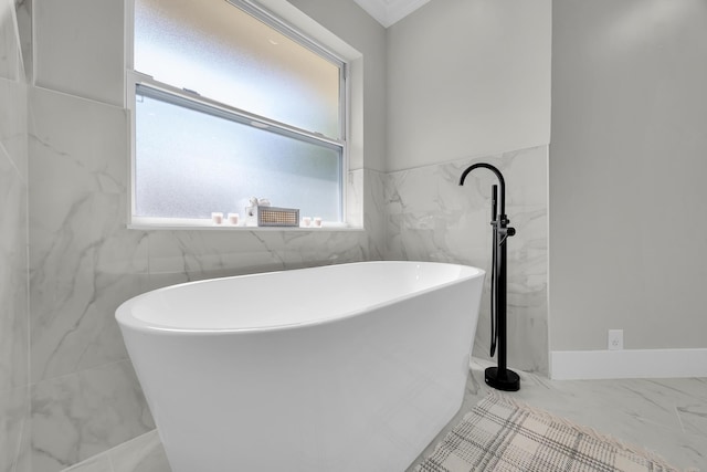 bathroom with marble finish flooring, tile walls, and a freestanding bath