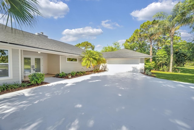 view of side of property featuring french doors, concrete driveway, and roof with shingles