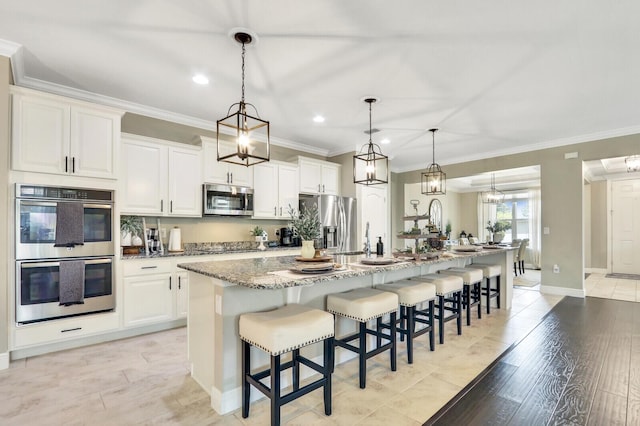 4052 SW Mccandless St, Port Saint Lucie, FL 34953 - kitchen featuring stainless steel appliances, a spacious island, ornamental molding, a kitchen bar, and white cabinetry