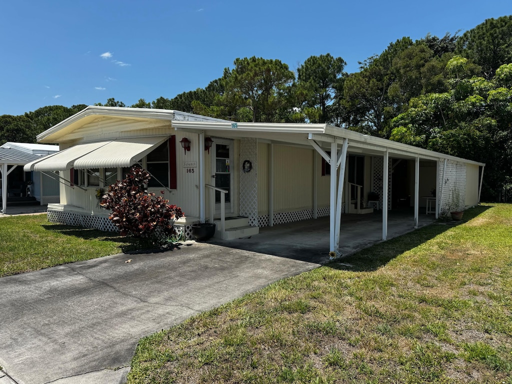 manufactured / mobile home featuring concrete driveway, a front yard, and a carport
