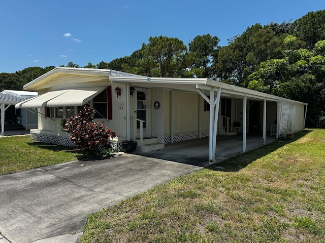 manufactured / mobile home featuring concrete driveway, a front yard, and a carport