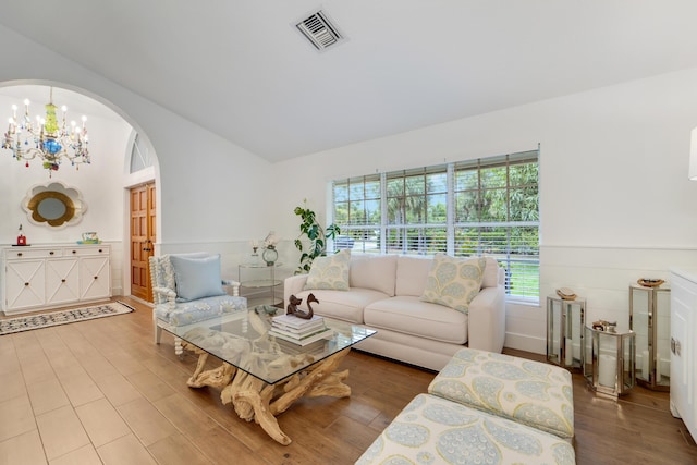 living room featuring arched walkways, plenty of natural light, a chandelier, wood finished floors, and vaulted ceiling