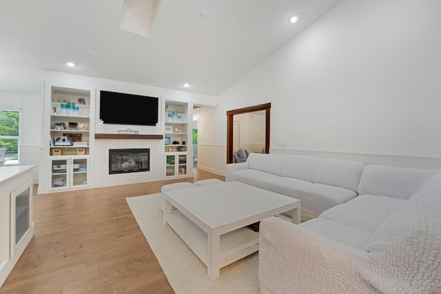 living room featuring a glass covered fireplace, light wood-style flooring, lofted ceiling, recessed lighting, and built in features
