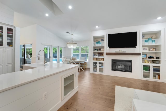 kitchen featuring wood finished floors, a sink, a glass covered fireplace, decorative light fixtures, and light countertops