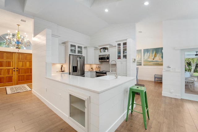 kitchen with appliances with stainless steel finishes, vaulted ceiling, light wood-style floors, a chandelier, and a peninsula