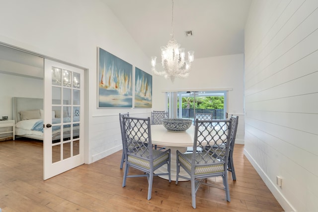 dining space with a chandelier, high vaulted ceiling, wood finished floors, and wooden walls