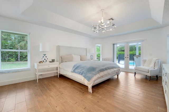 bedroom featuring a raised ceiling, a chandelier, french doors, and access to outside