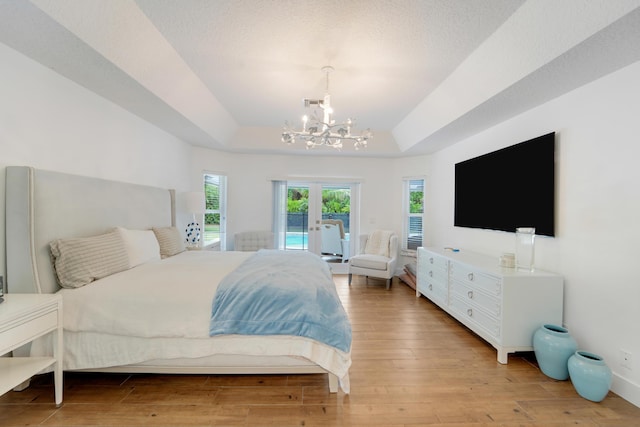 bedroom featuring access to exterior, a chandelier, a tray ceiling, and wood finished floors