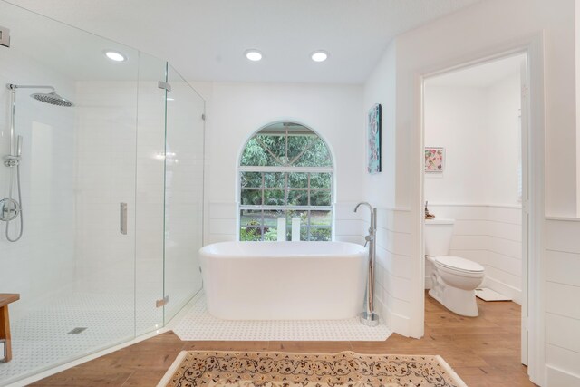 bathroom featuring wood finished floors, a shower stall, wainscoting, a soaking tub, and toilet