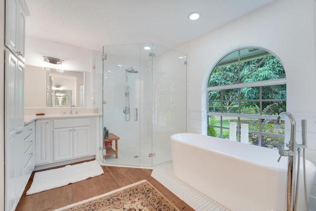 bathroom featuring vanity, a shower stall, wood finished floors, a soaking tub, and recessed lighting