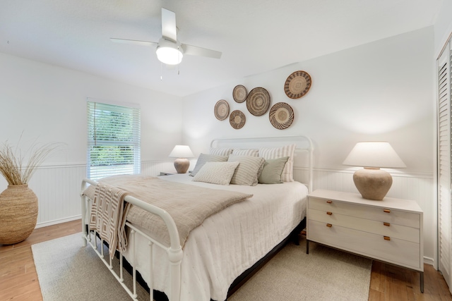 bedroom with wainscoting, light wood-style floors, and a ceiling fan