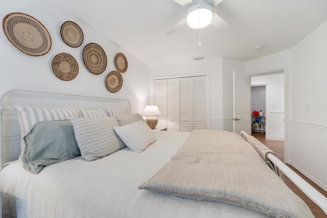 bedroom featuring wainscoting, a closet, wood finished floors, and ceiling fan