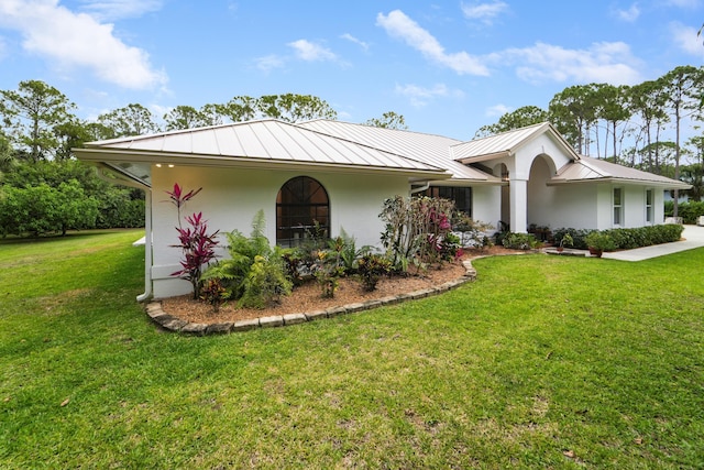 ranch-style home featuring a standing seam roof, a front yard, stucco siding, and metal roof