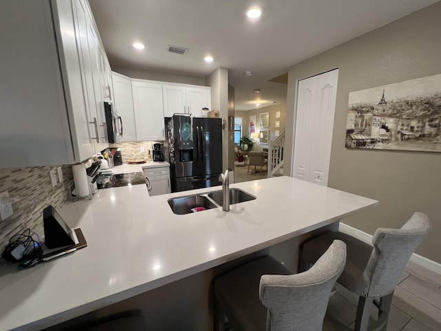 13044 Anthorne Ln, Boynton Beach, FL 33436 - kitchen with black fridge with ice dispenser, a peninsula, decorative backsplash, a sink, and a kitchen bar