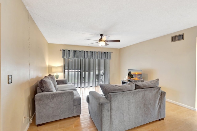 living area with ceiling fan, light wood-style flooring, baseboards, and a textured ceiling