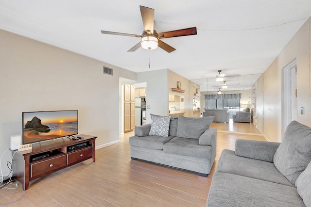 living room featuring ceiling fan, light wood-type flooring, and baseboards