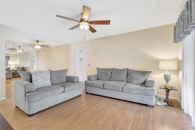living area featuring a ceiling fan, light wood finished floors, and baseboards
