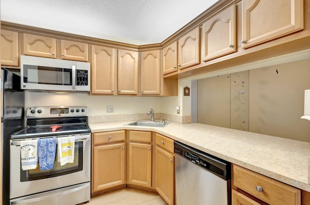 kitchen with appliances with stainless steel finishes, a sink, light brown cabinetry, and light countertops