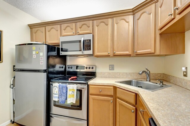 kitchen featuring appliances with stainless steel finishes, a sink, light countertops, light brown cabinets, and a textured ceiling